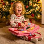 Dziecko siedzące pod choinką bawi się świąteczną tablicą edukacyjną Bzikotek i uśmiecha się z radości.